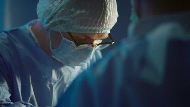 A close up shot of the surgeon wearing glasses and concentrating performing a surgery in a medical room