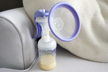 Breast pump containing breast milk sitting on a chair used to nurse a baby