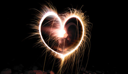 A woman is playing with hand-held fireworks by drawing hearts.
Happiness concept.