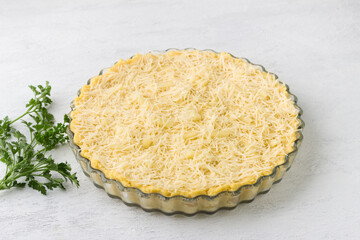 Raw polenta in a baking dish sprinkled with grated cheese and a bunch of parsley on a light gray background. Stage of cooking delicious Italian polenta