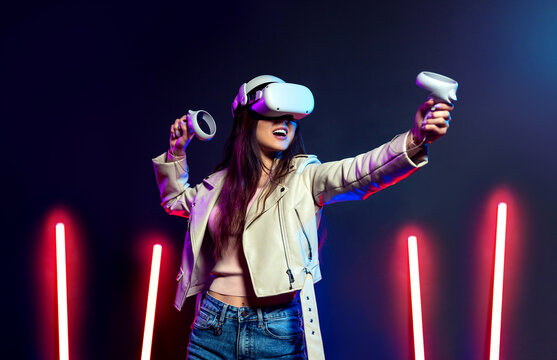 Happy girl playing virtual reality game in vr headset glasses in neon lights. Gamer in goggles with joysticks.