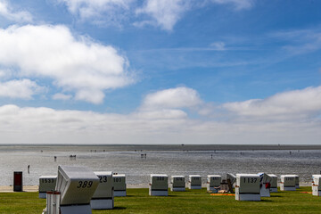 Vacation by the sea: beach chairs and people walking in the mudflats under a blue sky