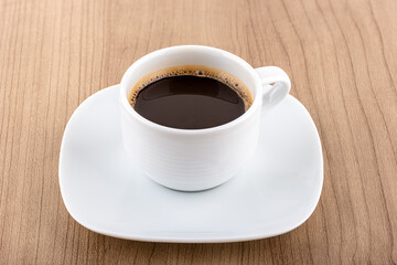 Black coffee in a white cup on a saucer over a wooden background.