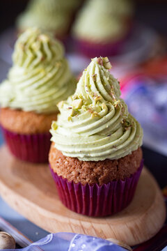 An exquisite dessert for a romantic breakfast: pistachio cupcakes with crushed pistachios on a wooden board. Vertical photo