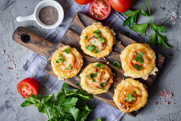 A hearty family lunch: mini pizzas with mozzarella, tomatoes, salami and fresh herbs on a wooden board on a gray background. view from above