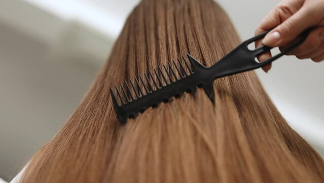 Back view of beautiful young woman in white undershirt combing her hair in bathroom. Woman combing long brown gray hair by brush, concept hair health, natural hair care