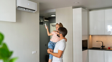 Father kept to hand little daughter and turn on air conditioner using remote control. Happy family...