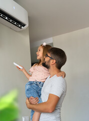 Happy family, father and little daughter fun turn on air conditioner using remote control. Cooler...