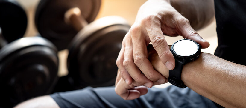 Sport man checking workout result on smartwatch app after weight training exercise in fitness gym. Wearable device or personal fitness tracker. Smart watch technology for health tracking and activity