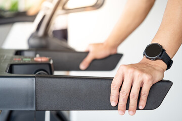 Runner man wearing smartwatch while using treadmill running in fitness gym. Wearable device for...