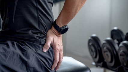 Sport man feeling lower back pain or spine pain after doing weight training exercise in fitness...