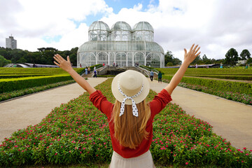 Tourism in Curitiba, Brazil. Back view of stylish traveler woman with raising arms in  botanical...
