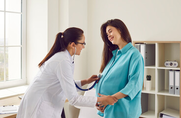 Happy pregnant woman has appointment with doctor at clinic. Female gynaecologist OB GYN medic specialist with stethoscope listens to baby's heartbeat in mother's belly. Pregnancy, health care concept