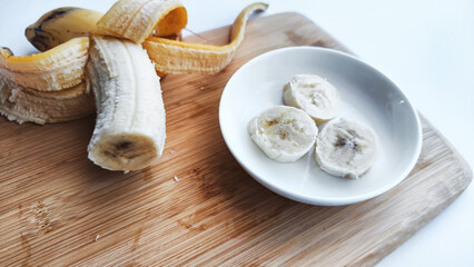 Banana with open panel on wooden board and sliced round pieces on the plate on white background. Ripe banana with peel and cooking, Close up. Delicious sweet fruit dessert