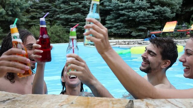 A group of young people refreshing in the swimming pool and toasting together with cold drinks.	

