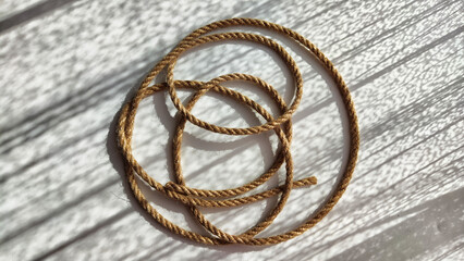 Jute twisted rope lying on a white surface with shadows from the sun. Abstract background, texture, pattern, frame