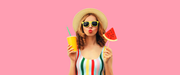 Summer colorful portrait of beautiful young woman blowing her lips with cup of juice and lollipop or ice cream shaped slice of watermelon wearing straw hat on pink background
