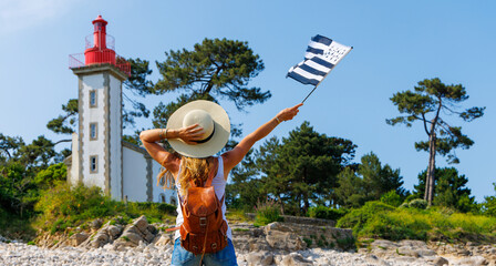 tourism in Brittany- Lighthouse on atlantic coast and woman tourist holding breton flag- Brittany in France (phare de Sainte Marine) - obrazy, fototapety, plakaty