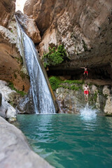 Naklejka premium man in red shorts jumping into the azure lake next to a waterfall in a canyon in desert