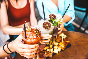 Happy friends clink cocktail glasses at bar restaurant - Young people enjoying happy hour toasting...