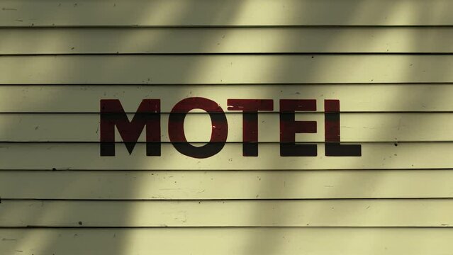 Shadow of palm leaf moving gently in wind on siding of motel with painted lettering  on wooden slats background, backdrop