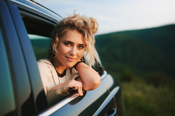 Fototapeta na wymiar Happy young blonde woman leaning out of the car window enjoying nature