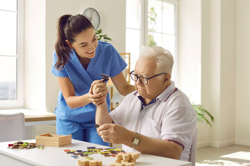 Fototapeta Friendly caregiver or nurse in geriatric clinic or retirement home helping senior patient with puzzle. Old man sitting at table and solving alphabet puzzle. Dementia, Alzheimer's disease concept obraz
