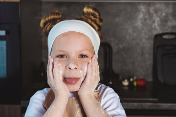 Cooking or Culinary school for children, kids. Little girl with hands and a face smeared in flour,...