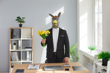Funny man in a suit wearing animal donkey mask on head standing in the office at his workplace with...