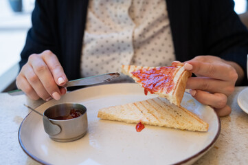 Close-up. Business woman spreads jam on toast in an outdoor cafe.