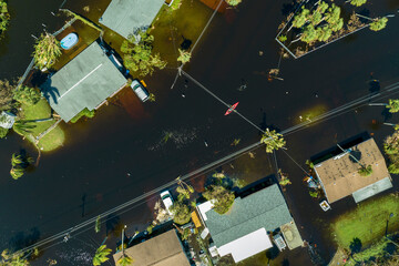 Aftermath of flooding natural disaster. Kayak boat floating on flooded street surrounded by...