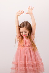 happy little girl with blonde hair and in a pink dress catches confetti on a white background, holiday concept