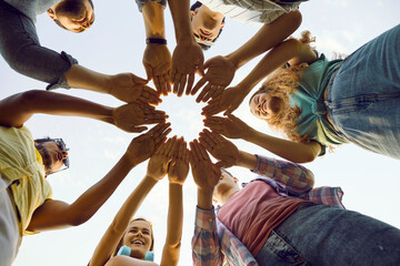 Group of friends stand outdoors making circle with their hands that symbolizes unity. Bottom view of hands of young happy people putting them together against background of sky. Concept of friendship.