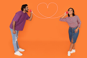 Young indian couple with can phone on orange background
