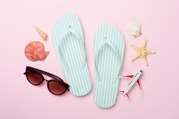 Flip flops with sunglasses and airplane on color background, top view