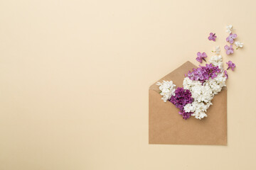 Envelop with lilac flowers on color background, top view