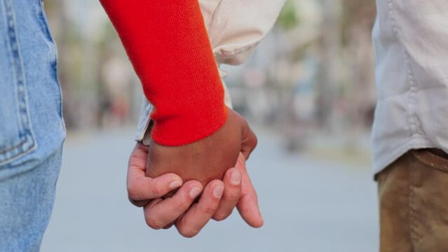 Close up slow motion of a young multiracial couple walking together and holding hands with affection. Union of married pair of people bonding on a tender and amorous relationship on a romantic dating