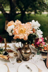 Obraz na płótnie Canvas coral and white peonies in an iron vase on the table. holiday outdoors. details of a table decorated with a bouquet of peonies. table setting example.