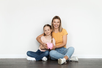 Fototapeta na wymiar Family Budget. Smiling Beautiful Mother And Little Daughter Holding Piggy Bank