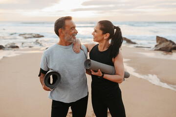 Smiling mature european couple in sportswear with mats enjoy workout together in morning on sea...