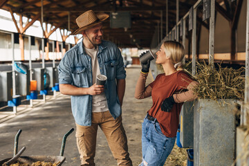 A male and female farmer are standing in the stall at the animal farm and talking.