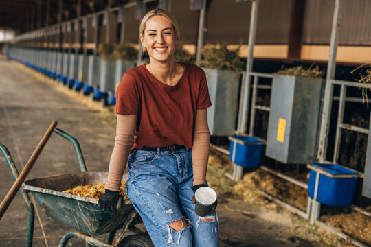 Portrait of a happy cowgirl sitting on a cart in a stall.