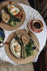 breakfast for two top view. fried eggs with asparagus, herbs and a piece of sourdough bread. healthy and nutritious breakfast with black coffee.