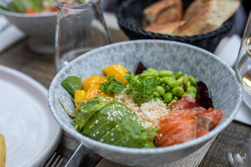 Healthy salad of greens, avocado, beans, mango, rice and fish with pinch of sesame seeds on top in deep bowl on table.