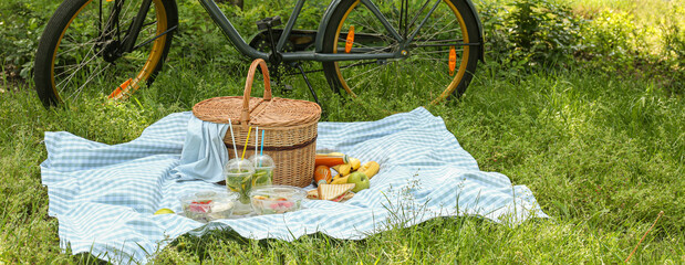 Wicker basket with tasty food and drink for romantic picnic on plaid in park