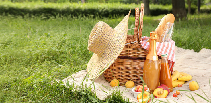 Wicker basket with hat, tasty food and drinks for romantic picnic in park
