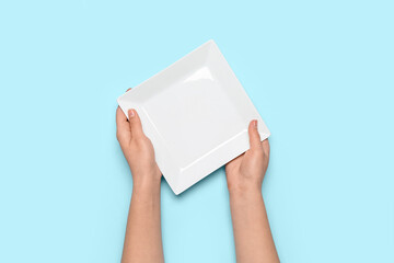 Female hands with empty plate on blue background