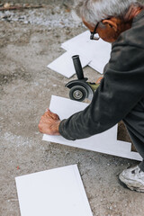 A man, a worker in a robe in an outdoor workshop, cuts off a plastic white material for insulation with a grinder, an electric cutter. Close-up photography, industry.
