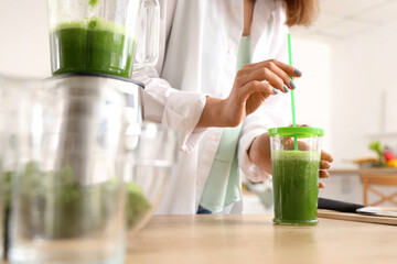 Young woman with glass of vegetable juice in kitchen, closeup