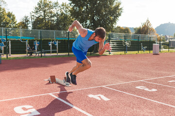 Young man training for run race start on a stadium track outside